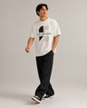 Man wearing a white t-shirt with a logo and black pants on a plain background