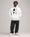 Person wearing a white hoodie with a logo and text, standing against a plain background
