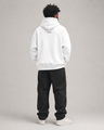 Person wearing a white hoodie and black pants on a gray background