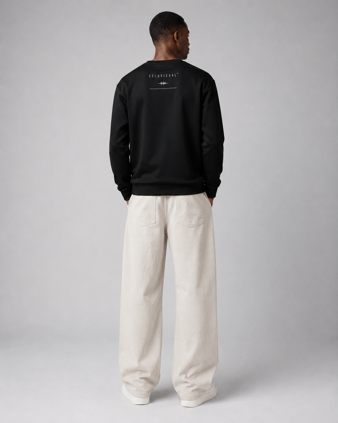 Person wearing a black sweatshirt with text on the back, standing against a plain background
