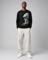 Person wearing a black sweatshirt with a white graphic design and white pants on a gray background