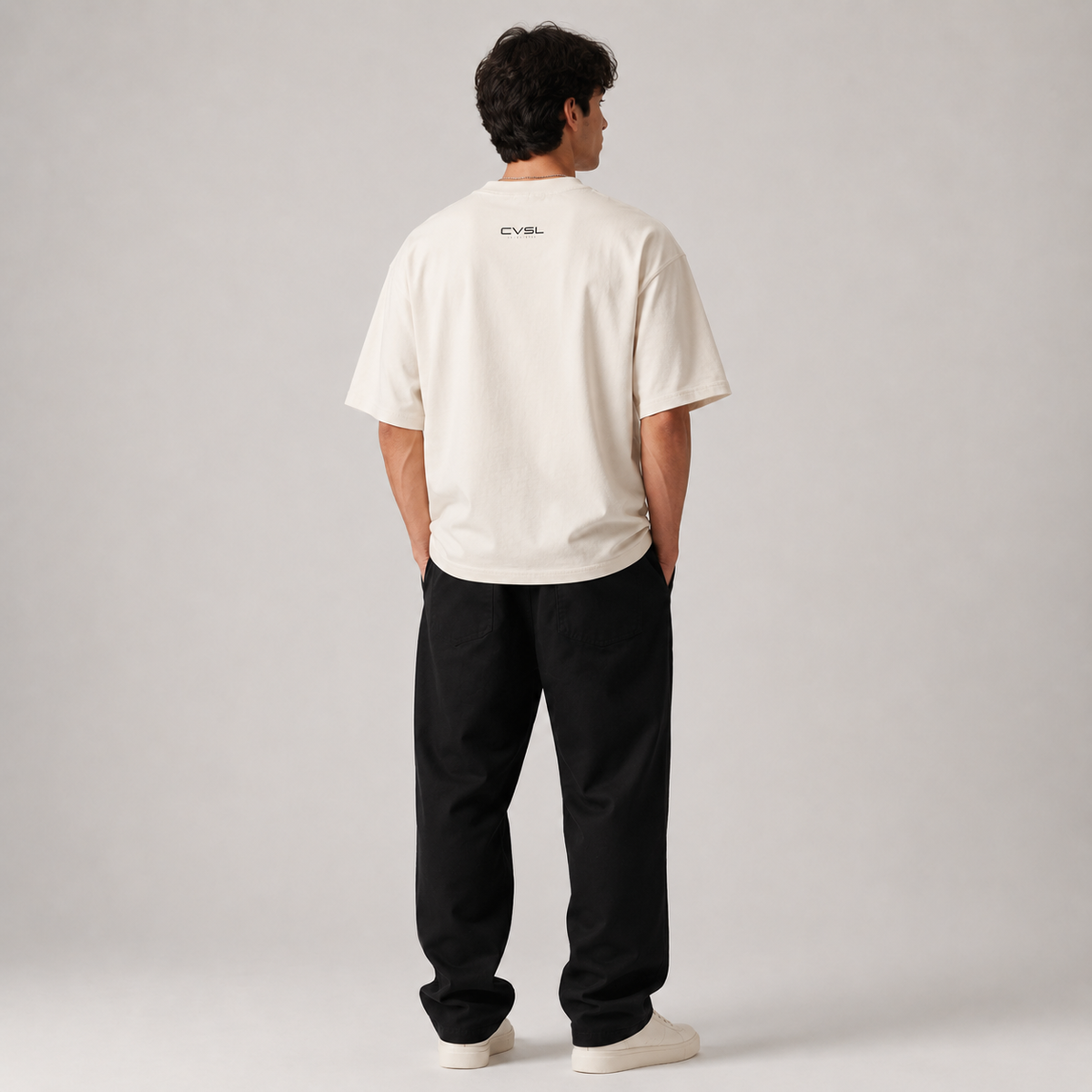Person wearing a white t-shirt with text on the back and black pants against a gray background