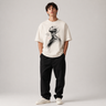 Person wearing a white t-shirt with a graphic design and black pants on a plain background
