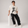 Person wearing a white t-shirt with black graphic design, sitting on a white box against a light gray background.