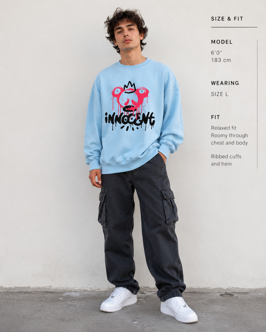 Person wearing a light blue sweatshirt with a graphic design and text, standing against a plain background.