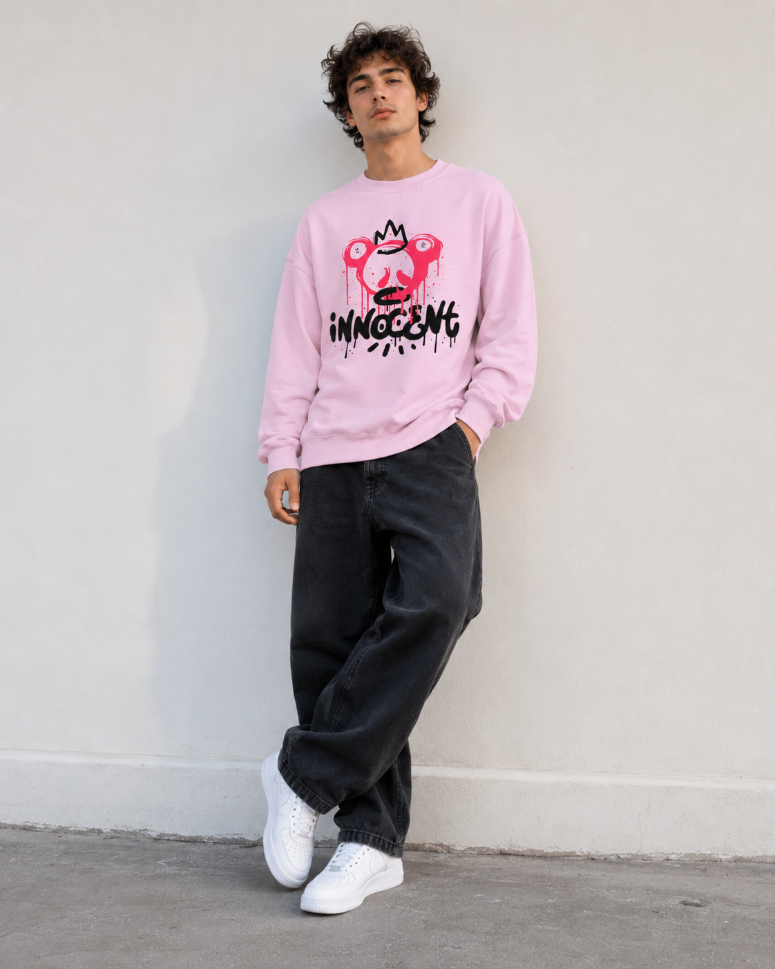 Person wearing a pink sweatshirt with a graphic design against a white wall