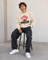 Person wearing a beige sweatshirt with a graphic design sitting on a stool against a plain wall.