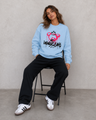 Person wearing a light blue sweatshirt with a graphic design sitting on a stool against a plain background