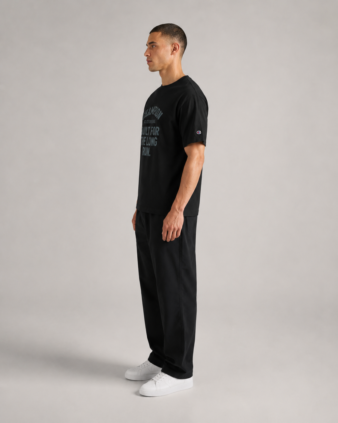 Man wearing a black t-shirt and pants standing against a gray background