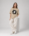 Person wearing a beige t-shirt with text and white pants on a plain background