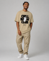 Man wearing a beige t-shirt with 'Chill Brew Club' text and cargo pants on a gray background