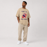 Man wearing a beige t-shirt with graphic design and text, standing against a plain background