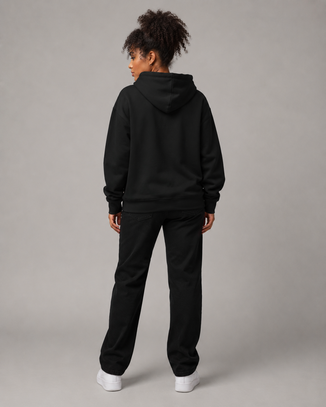 Person wearing a black hoodie and pants set on a gray background