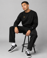 Person wearing a black sweatshirt and pants sitting on a stool against a gray background
