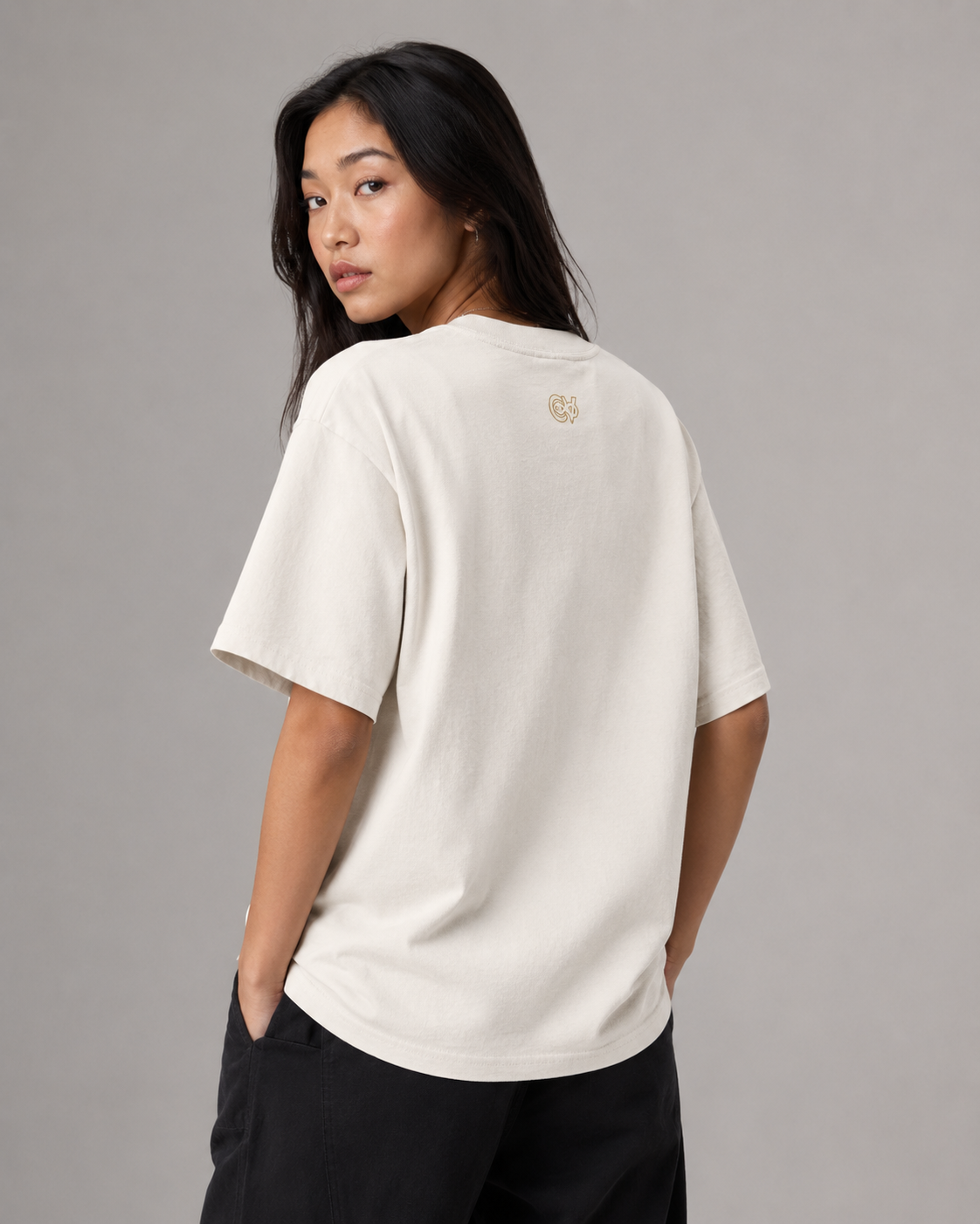 Woman wearing a beige t-shirt with a logo on the back against a gray background