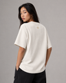 Woman wearing a beige t-shirt with a logo on the back against a gray background