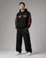 Person wearing a black hoodie with red and white designs on a gray background