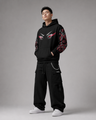 Person wearing a black hoodie and pants with red and white designs on a gray background