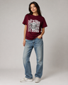 Person wearing a maroon t-shirt with graphic design and text, paired with blue jeans on a plain background