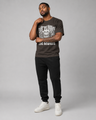 Man wearing a black t-shirt with graphic design and text, black pants, and white sneakers on a gray background