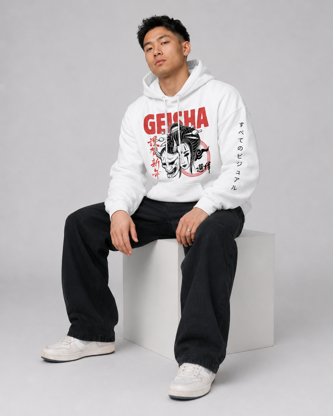 Person wearing a white hoodie with 'GEISHA' design, sitting on a white block against a gray background
