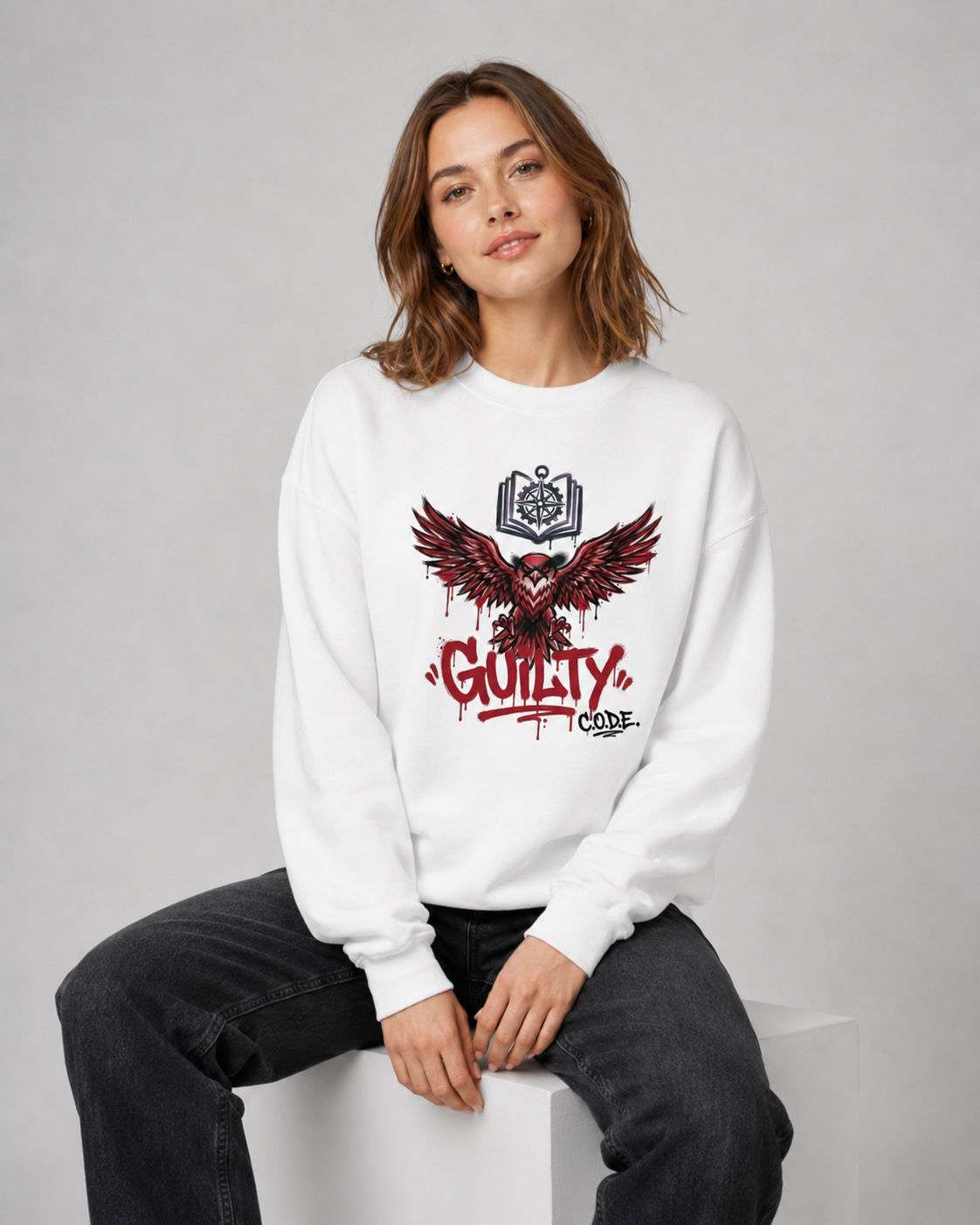 Person wearing a white sweatshirt with a graphic design and text, sitting on a white stool against a gray background.