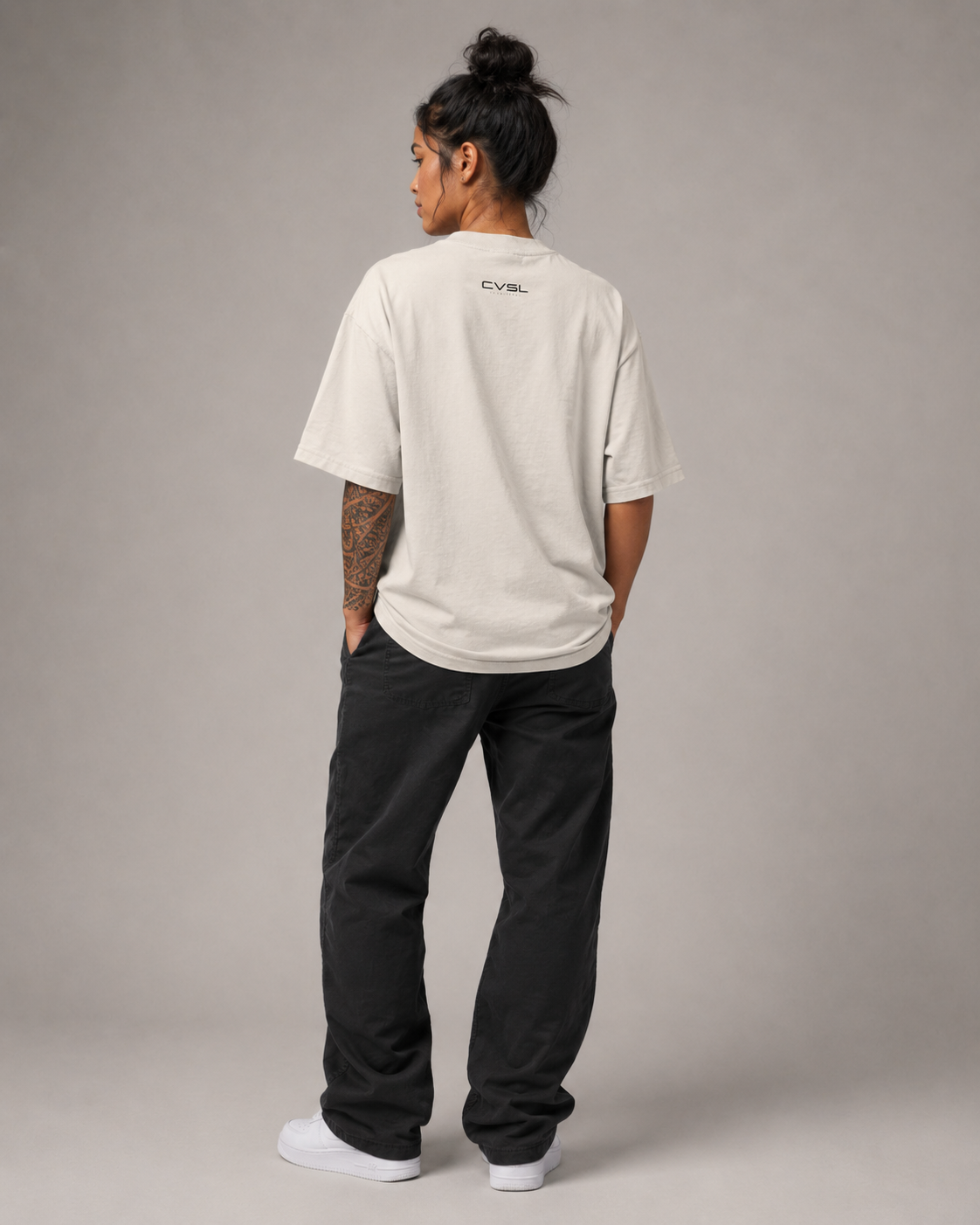 Person wearing a beige t-shirt and black pants on a gray background