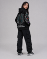 Person wearing a black hoodie with geometric designs and text, standing against a gray background