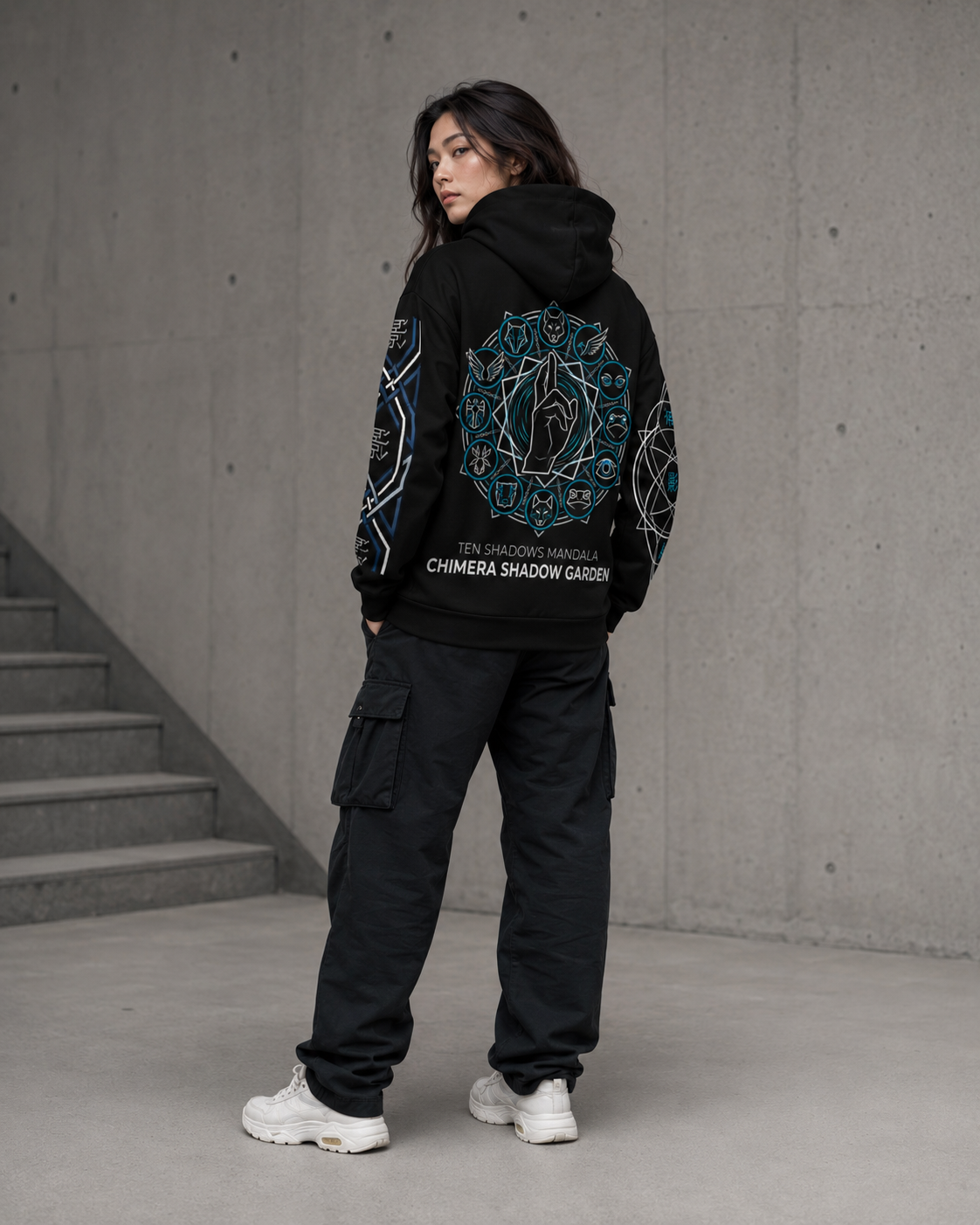 Person wearing a black hoodie with a geometric design and text, standing against a concrete wall.