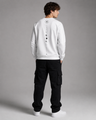 Person wearing a white sweatshirt with buttons and black cargo pants on a gray background