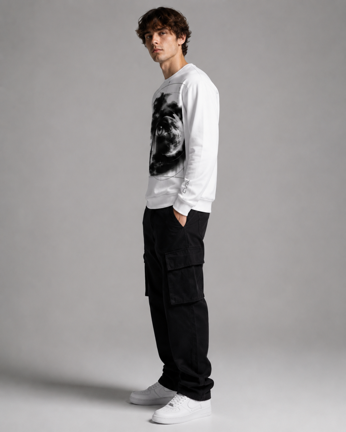 Man wearing a white sweatshirt with a graphic design and black cargo pants on a gray background