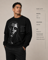 Man wearing a black sweatshirt with a graphic design and text, standing against a beige background.