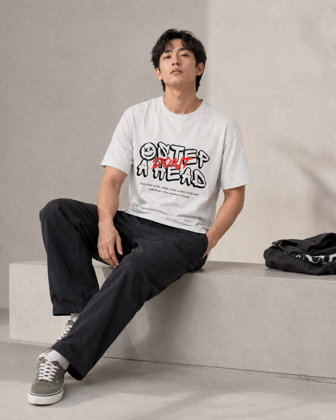 Person wearing a white t-shirt with text and graphics, sitting on a concrete bench.