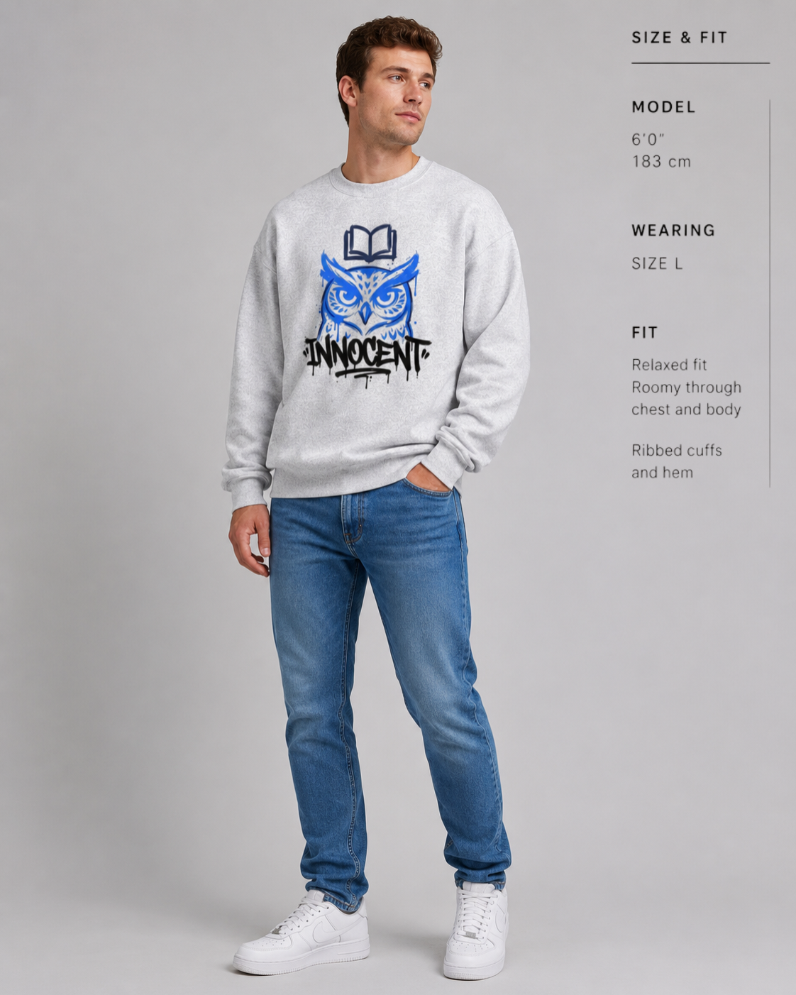 Man wearing a gray sweatshirt with a blue and black graphic design and blue jeans on a gray background.