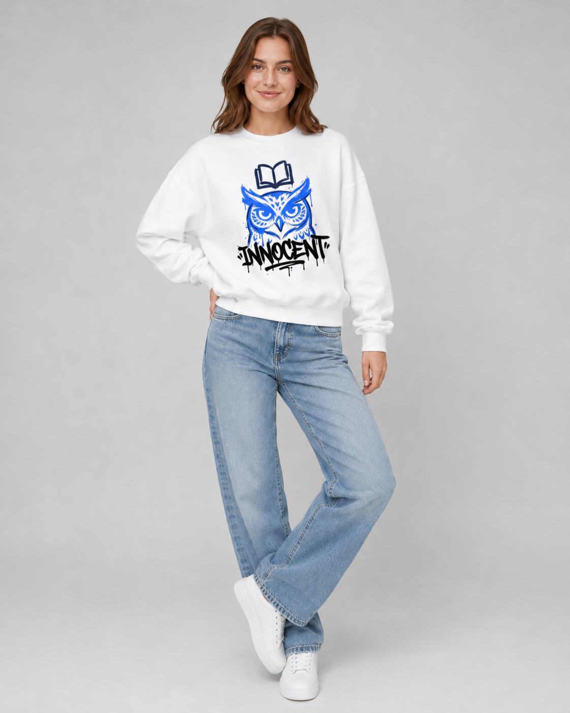 Woman wearing a white sweatshirt with a blue owl design and 'INNOCENT' text, paired with light blue jeans on a gray background.