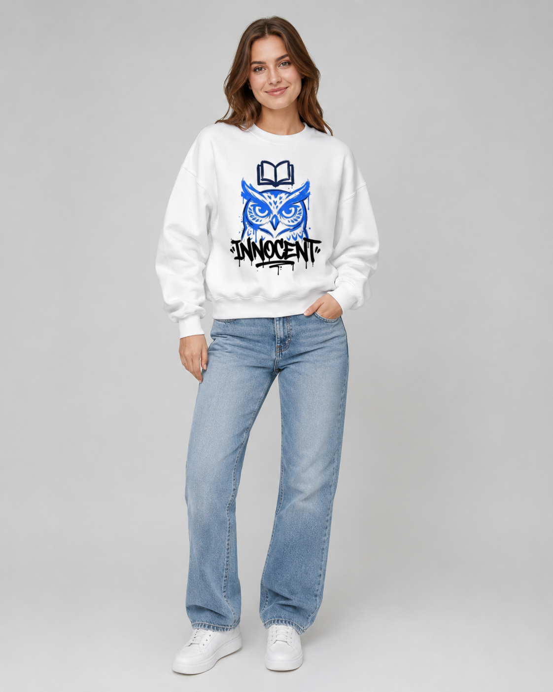 Woman wearing a white sweatshirt with a blue owl design and text, paired with light blue jeans on a gray background.