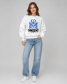 Woman wearing a white sweatshirt with a blue owl design and text, paired with light blue jeans on a gray background.