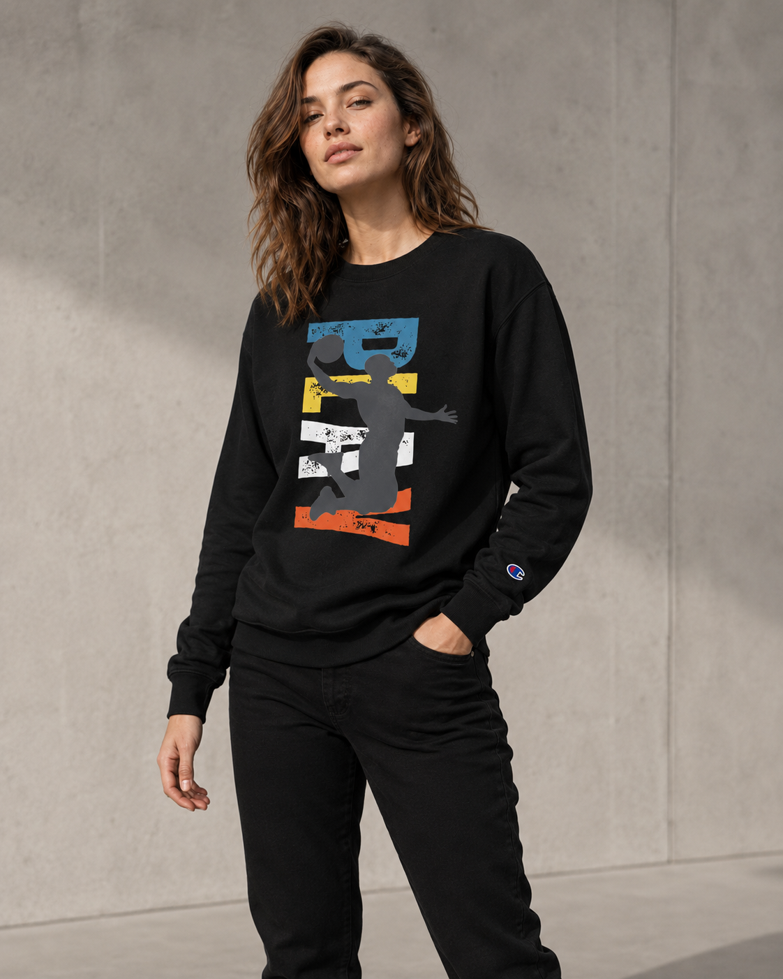 Woman wearing a black sweatshirt with a colorful graphic design against a gray concrete wall.