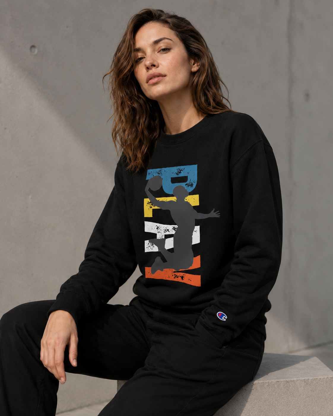 Woman wearing a black sweatshirt with colorful graphic design against a gray concrete wall.