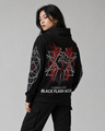 Person wearing a black hoodie with a red and white design on the back, standing against a gray background.