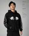 Person wearing a black hoodie with white graphic design on sleeves against a gray background