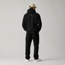 Person wearing a black hoodie and pants with a logo on the back, standing against a plain background.