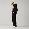 Person wearing a black hoodie and pants with a beige cap on a gray background