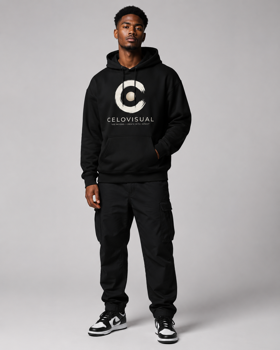 Person wearing a black hoodie with a logo and text, standing against a gray background