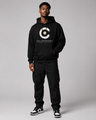 Person wearing a black hoodie with a logo and text, standing against a gray background