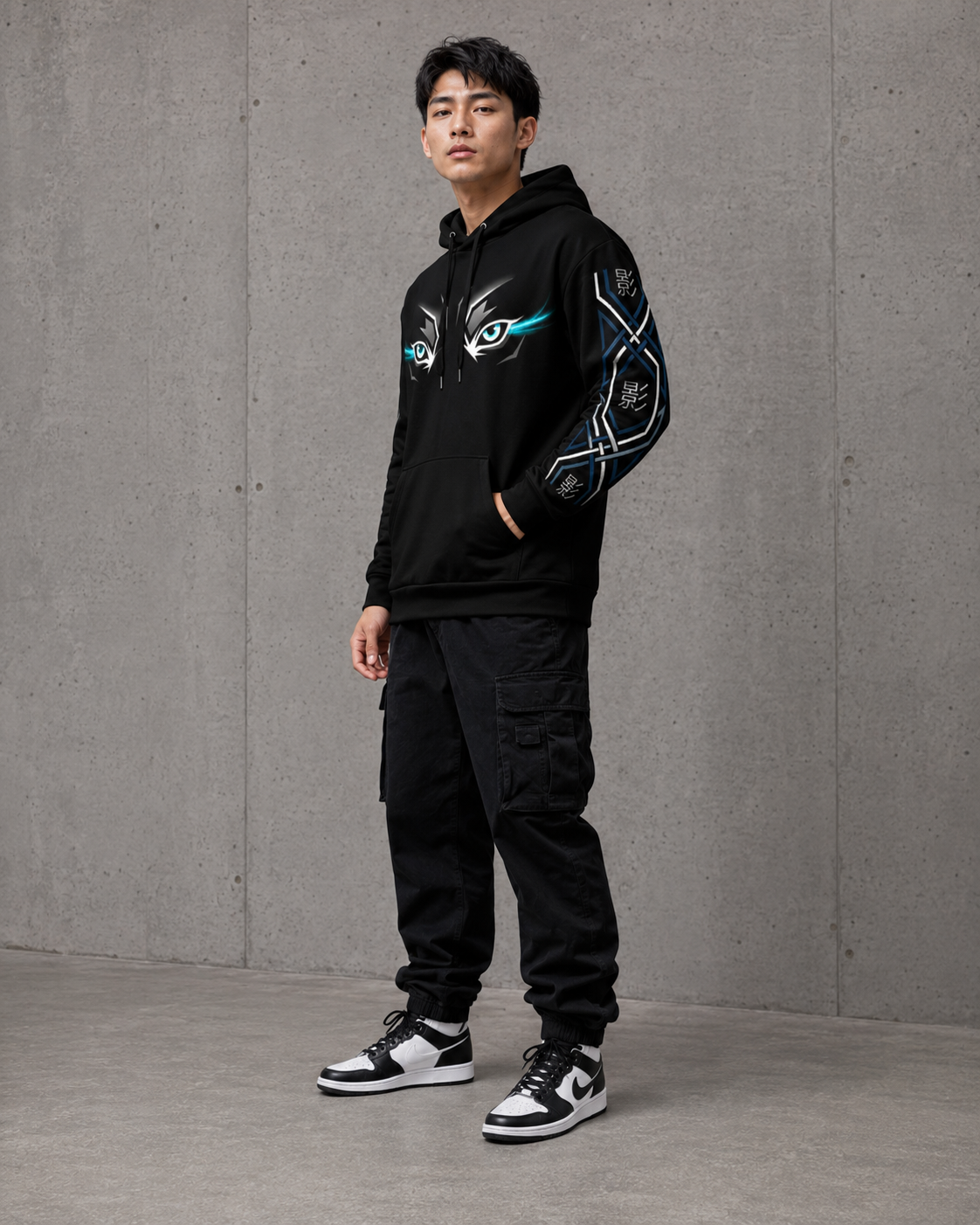 Person wearing a black hoodie and pants with unique designs, standing against a gray concrete wall.