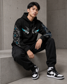 Person wearing a black hoodie with geometric designs sitting on a concrete surface.