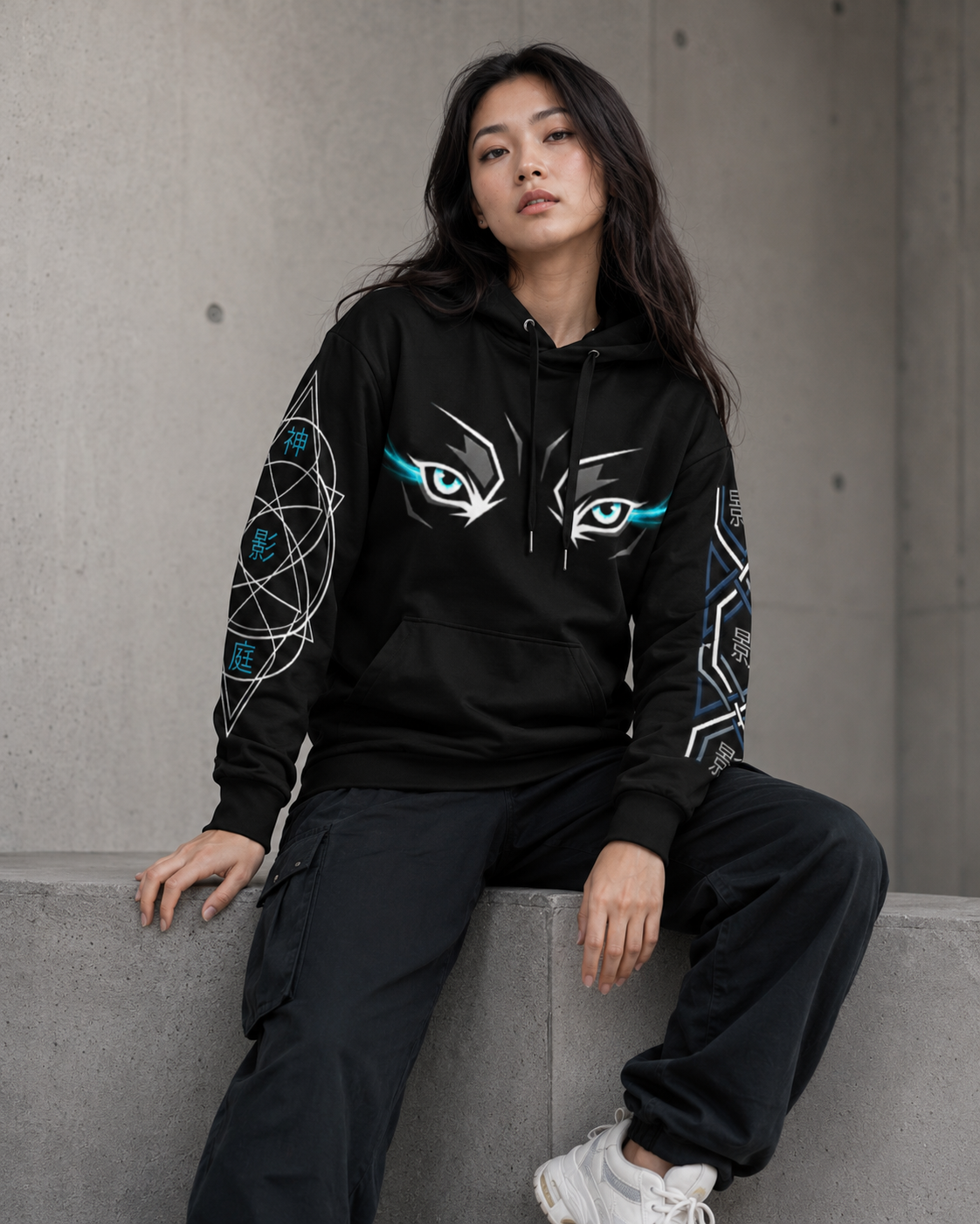 Person wearing a black hoodie with eye designs sitting on a concrete ledge.