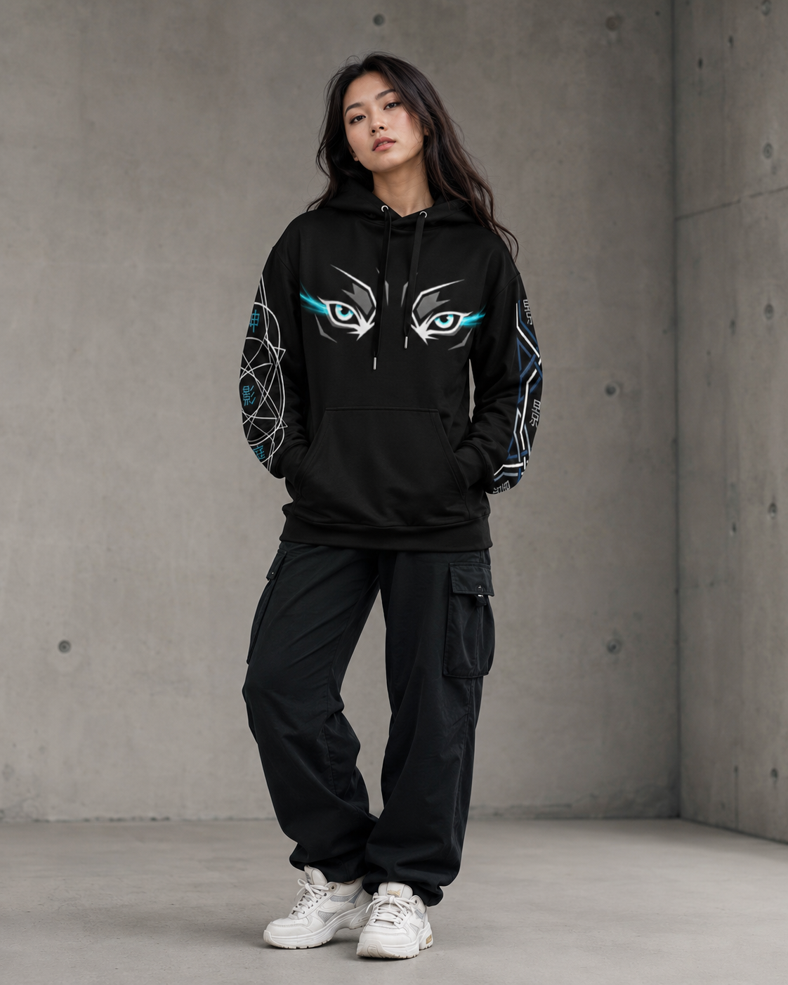 Person wearing a black hoodie with eye design and matching pants against a concrete wall.
