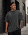 Man wearing a dark gray t-shirt with text standing against a modern building.